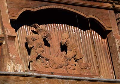 Balkon mit reich geschnitzten Figuren an einem Bauernhof in Grünenbach - Detail Holzer mit Zweimann-Zugsäge Schrot Säge Waldsäge