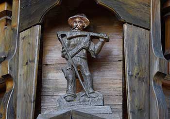 Balkon mit reich geschnitzten Figuren an einem Bauernhof in Ussenburg - Detail Mann mit Sense